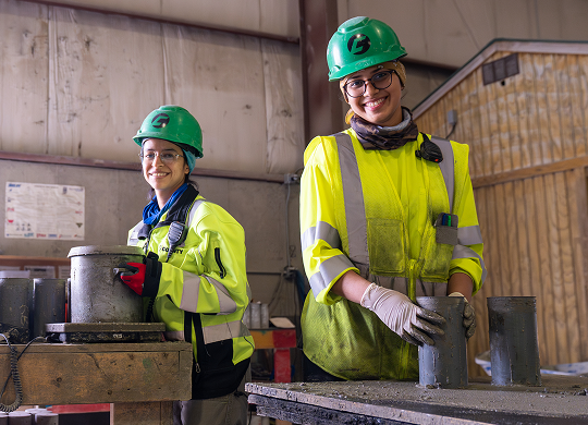 Two County Materials team members in safety gear working in a concrete manufacturing facility, representing women in manufacturing careers.