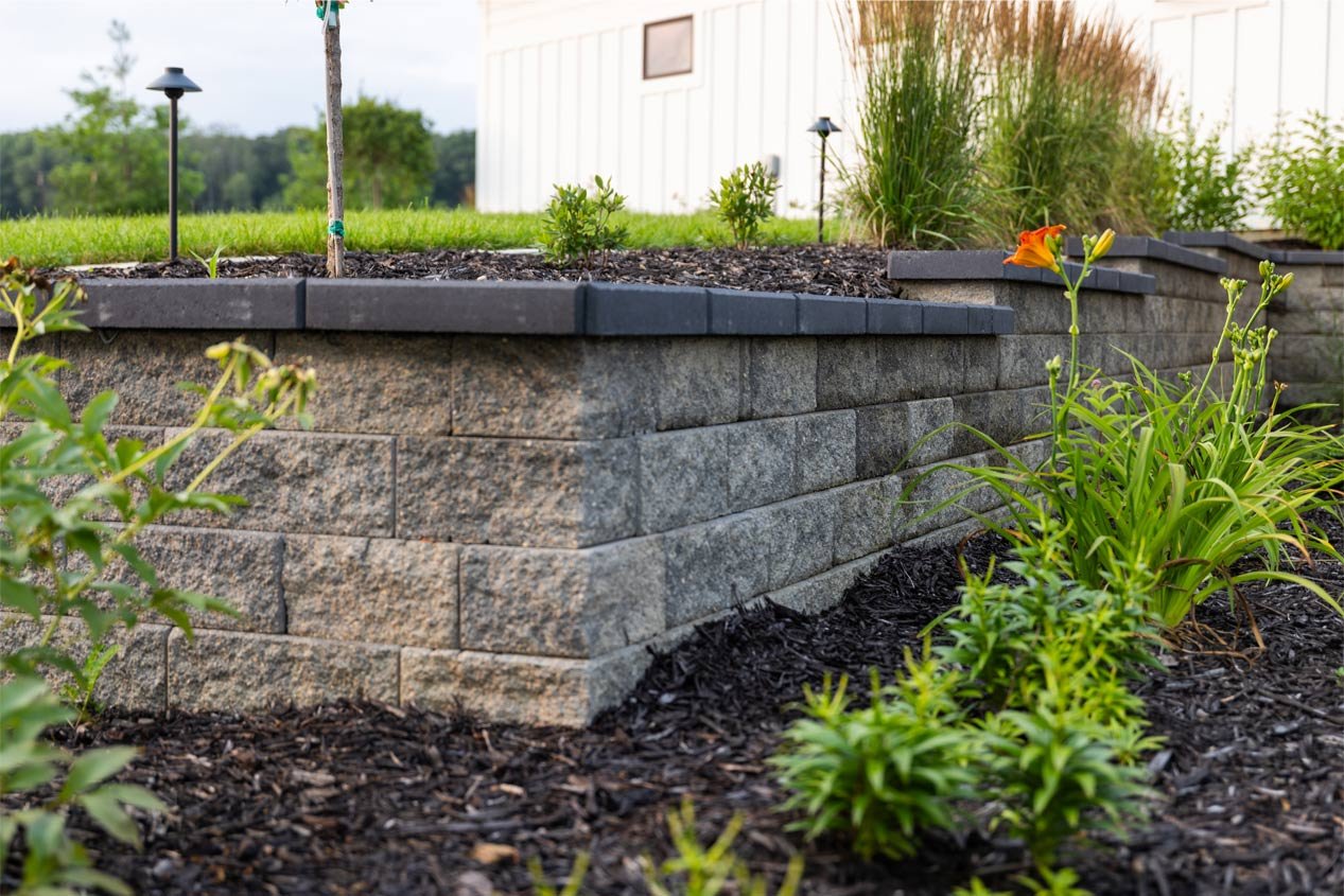 Close-up shot of a retaining wall outside corner with tan-colored retaining wall blocks and gray wall caps.