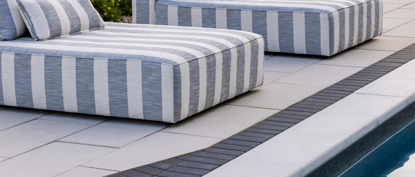Close-up of white concrete pool coping pavers and a paver pool deck with a contrasting border.