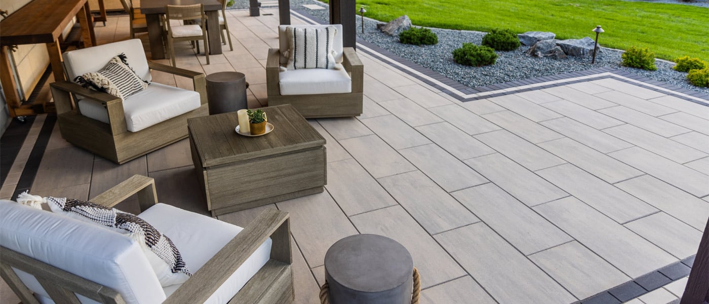 An intimate outdoor living area sits on a patio built with oversized smooth surface pavers in a light beige color with a charcoal inset border pattern. 